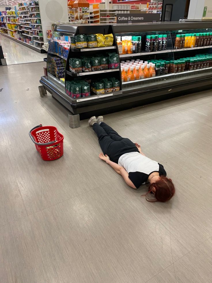 a person laying on the ground in front of a grocery store aisle with an empty shopping cart