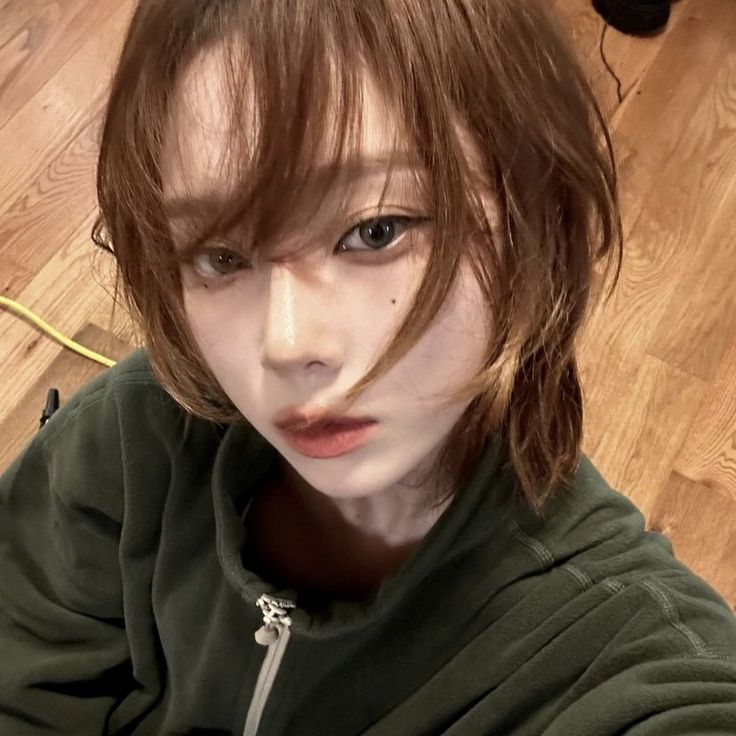 a young woman with brown hair and bangs posing for the camera in front of a wooden floor