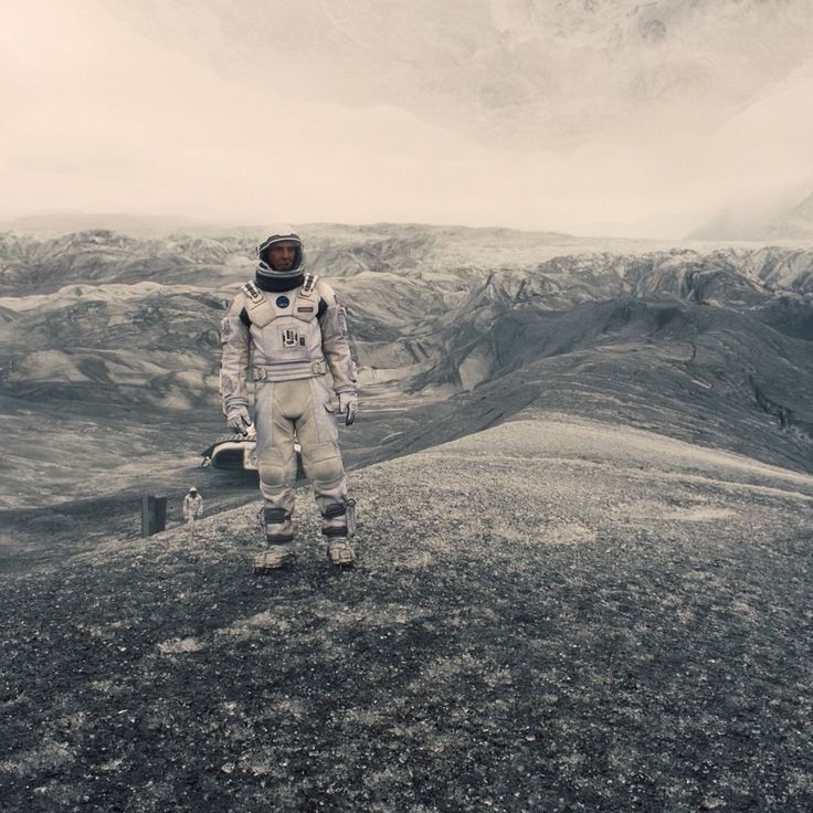 a man in an astronaut suit standing on top of a mountain with mountains in the background