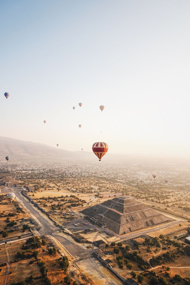 hot air balloons flying over the pyramids and desert landscape at sunrise or sunset in mexico