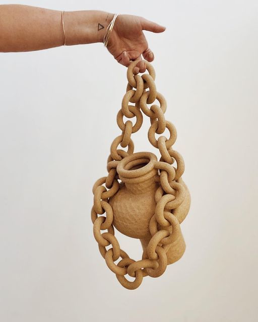 a hand holding a wooden chain with a vase on it's end and a pot in the middle