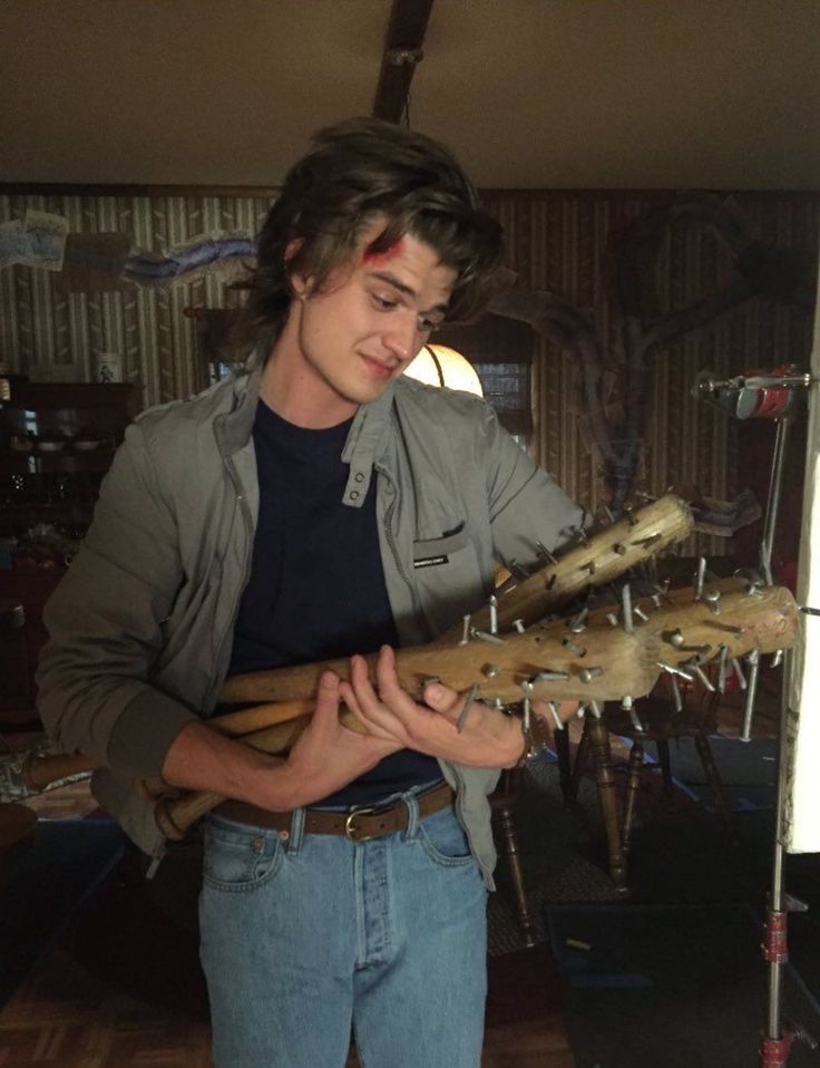 a young man holding two baseball bats in one hand and looking down at the other