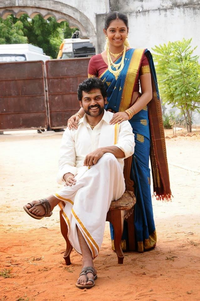 a man and woman sitting on a bench in front of a building, posing for the camera