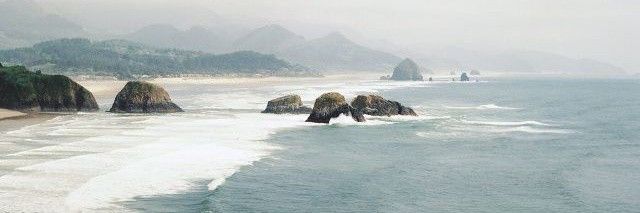 an aerial view of the beach and ocean with rocks in the water, on a foggy day