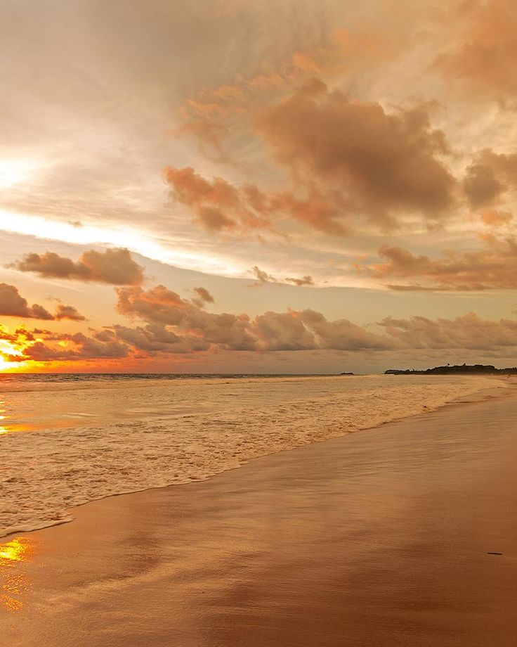 the sun is setting at the beach with waves lapping in front of it and some clouds