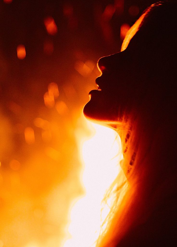 the silhouette of a woman's head in front of a fire