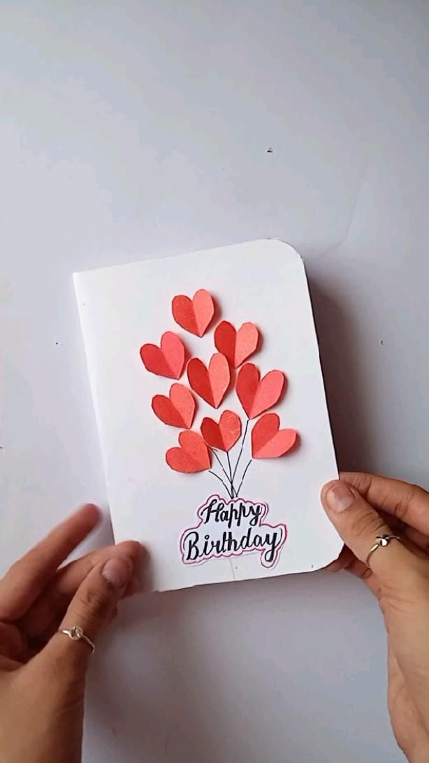 two hands holding up a card with hearts on it and the words happy birthday written on it