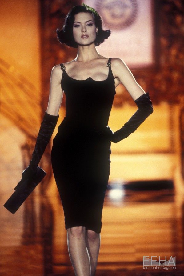 a woman in black dress and gloves walking down the runway