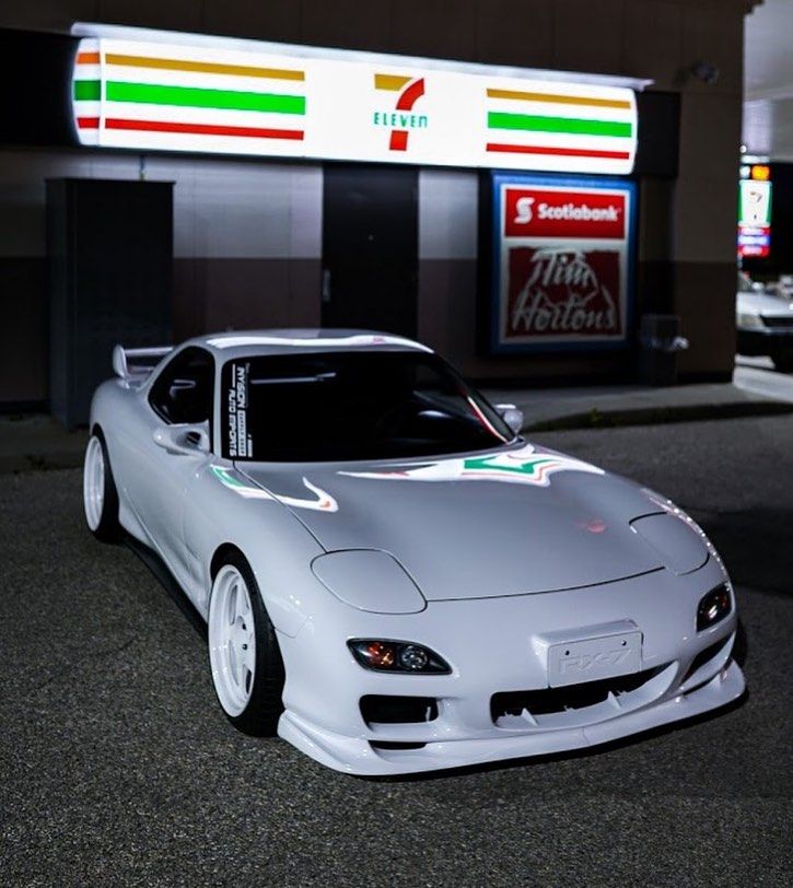 a silver sports car parked in front of a gas station at night with lights on