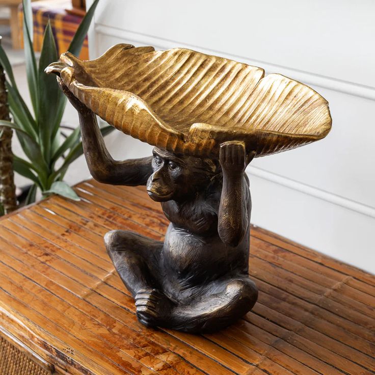 a bronze monkey holding a tray on its head sitting on top of a wooden table