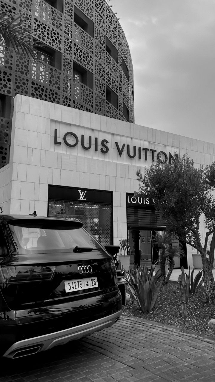 a black and white photo of a car parked in front of a louis vuitton store