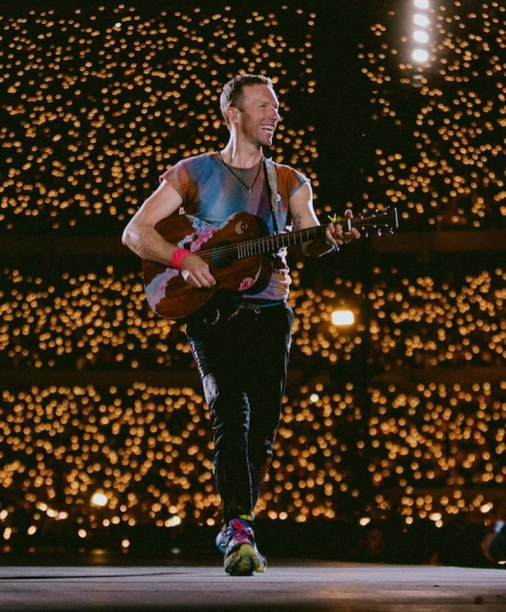 a man is playing an acoustic guitar in front of a large display of christmas lights