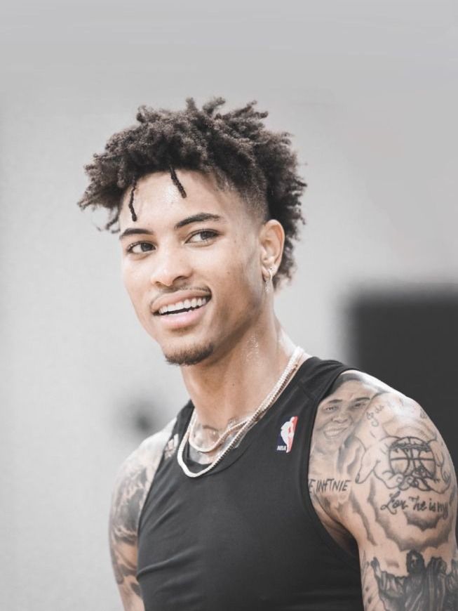 a young man with tattoos on his arm and chest smiles at the camera while wearing a black tank top