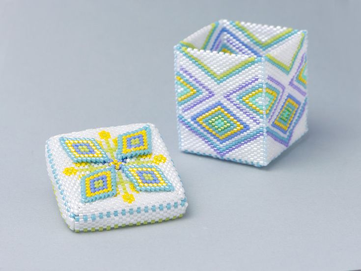 two small square beaded objects sitting on top of a gray surface, one with yellow and blue designs