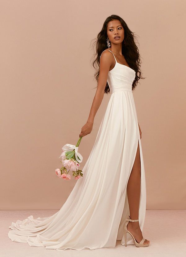 a woman in a long white dress holding a bouquet and posing for the camera with her legs crossed