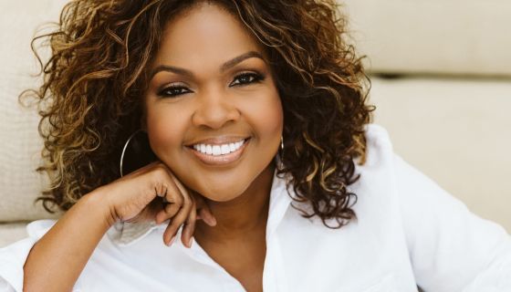 a woman sitting on top of a white couch smiling at the camera with her hand under her chin