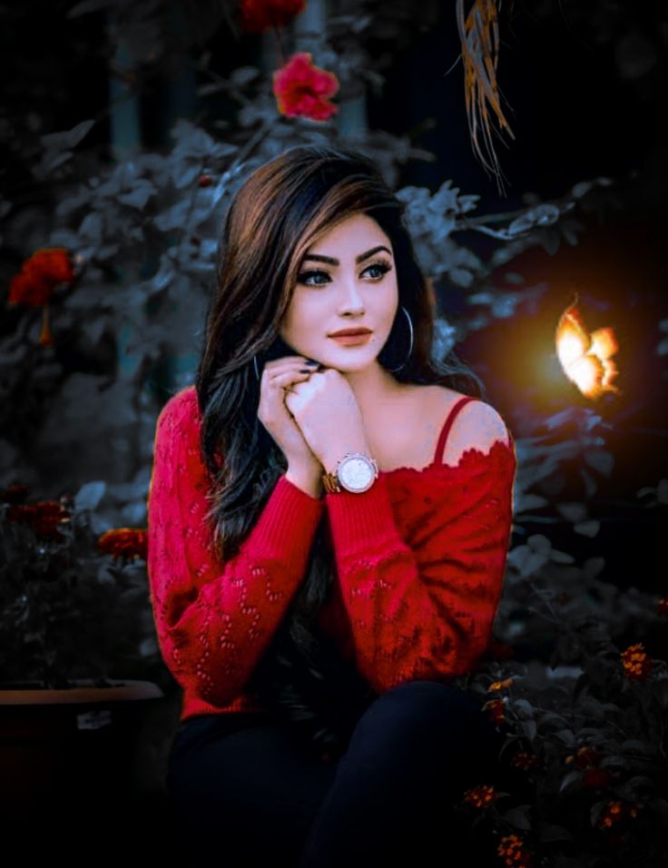a woman with long black hair wearing a red sweater and sitting in front of flowers