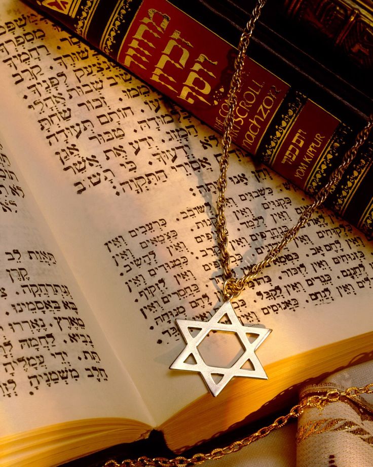 an open book with a silver star of david on it next to a chain necklace