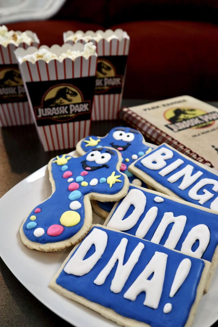 three decorated cookies sitting on top of a white plate next to boxes of popcorns