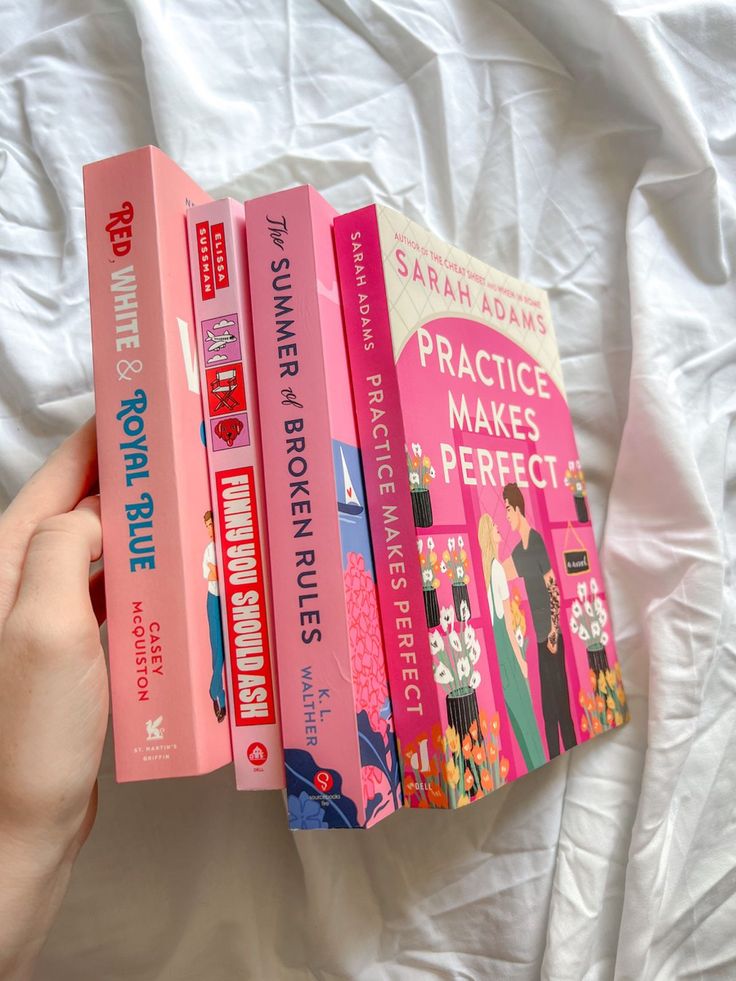 a person is holding three books in their hand on a white sheeted bed spread