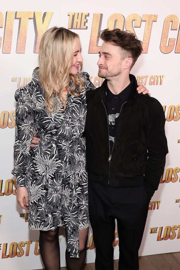 a man and woman standing next to each other on a red carpet in front of a movie poster