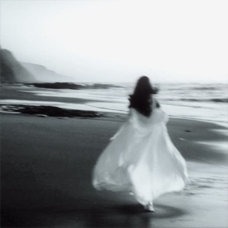 a woman is walking along the beach in a white dress