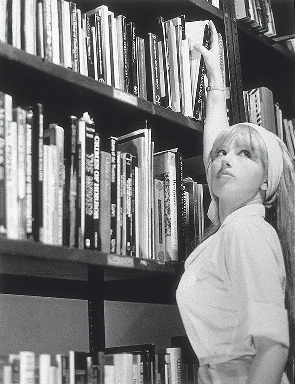 a woman reaching up to reach books on a book shelf in front of a row of books