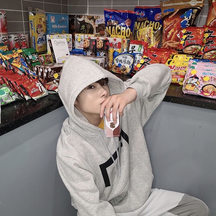 a person sitting on the ground in front of some snacks and candy bar bags, with one hand up to their face