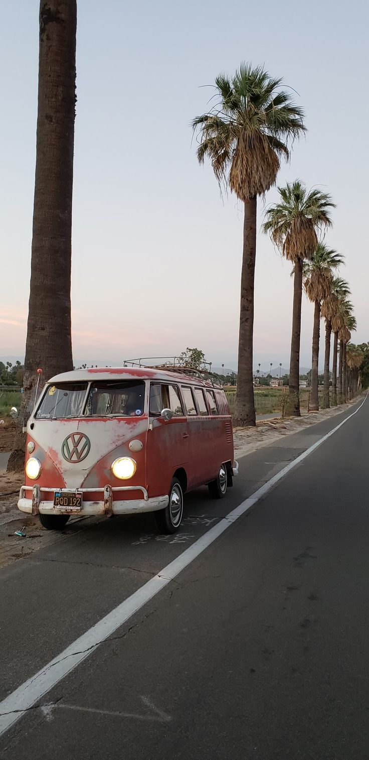 an old vw bus is parked on the side of the road in front of palm trees