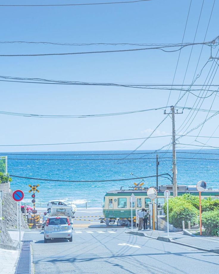 cars are driving down the road near the ocean and beach side houses with power lines above them