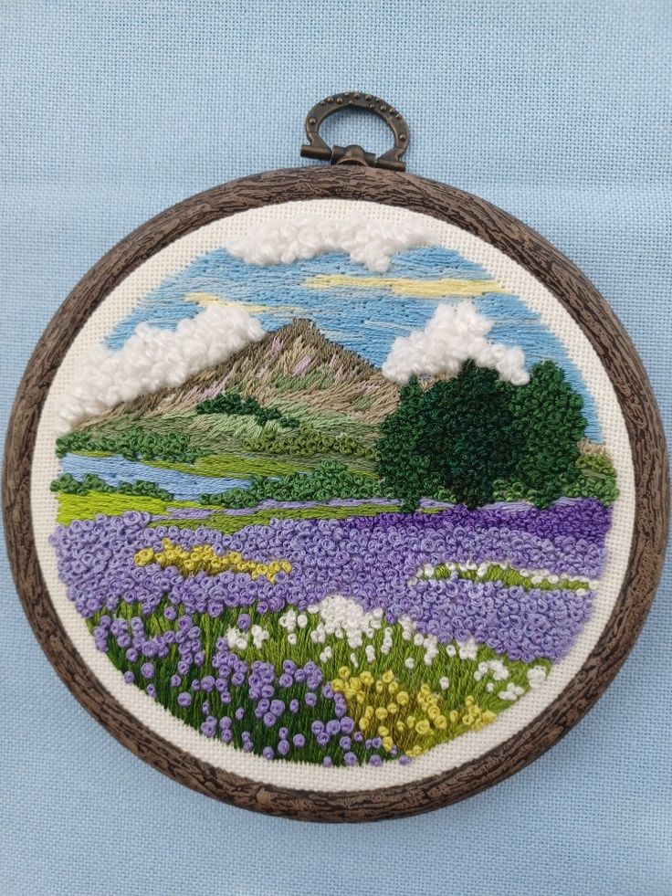 a hand embroidered ornament with purple flowers and mountains in the background on a blue fabric