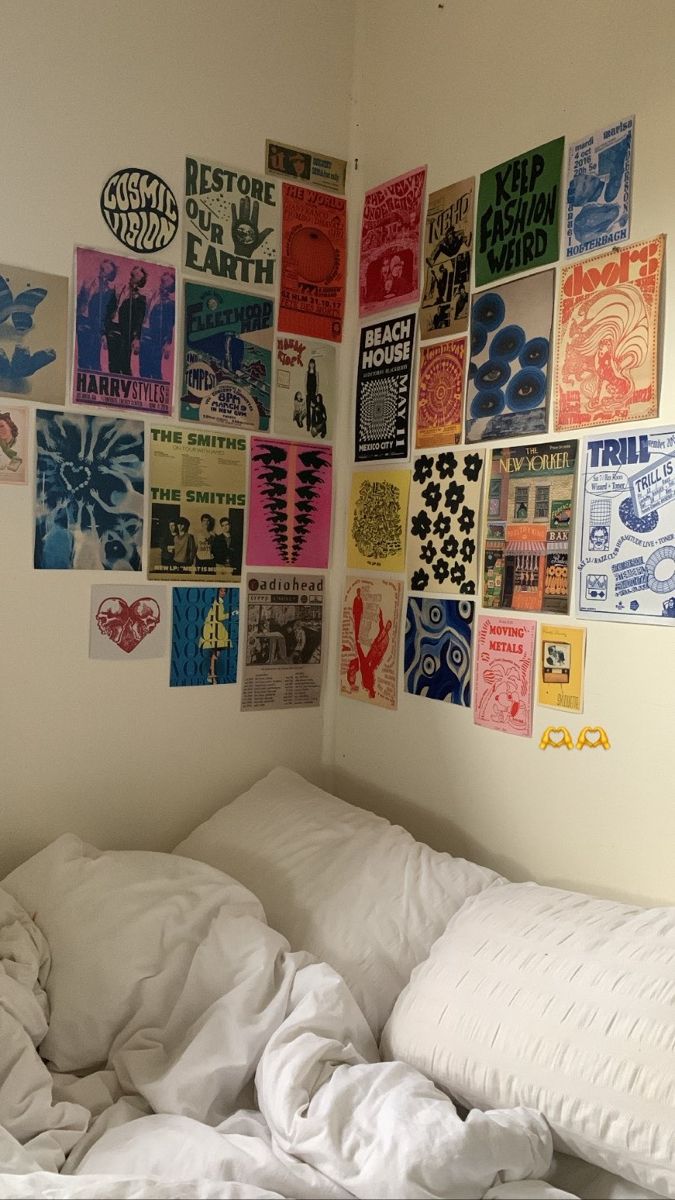 an unmade bed with white sheets and posters on the wall