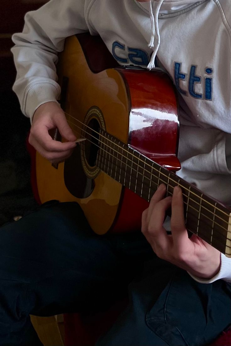 a young man is playing the guitar in front of his face while wearing a hoodie
