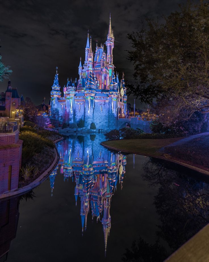 the castle is lit up at night with its lights on and reflecting in the water