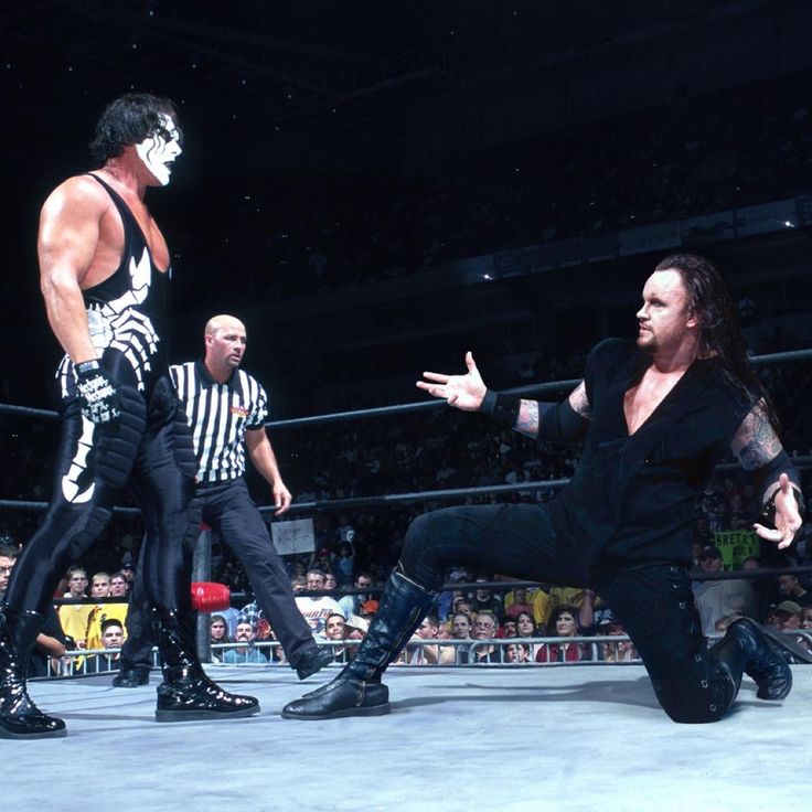 two men in black wrestling outfits and one is holding his hand out to the other man