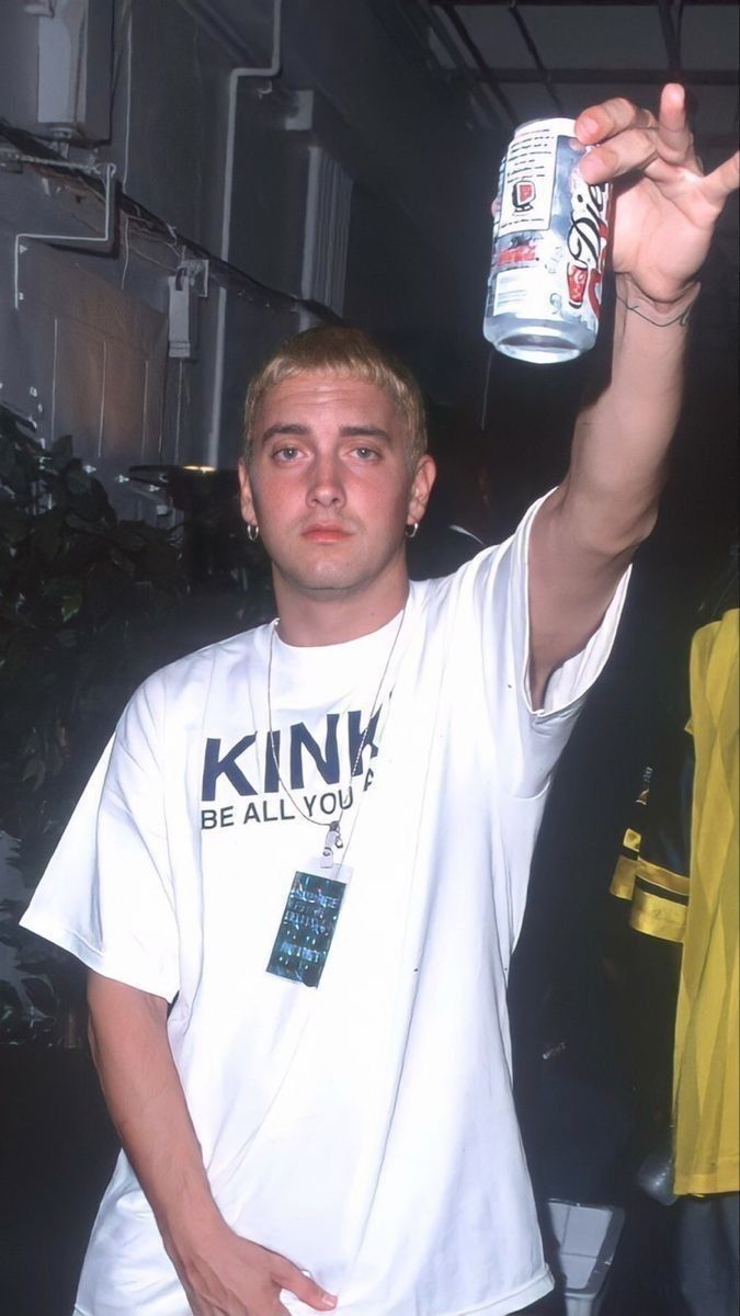 a young man holding up a can of beer in his hand and wearing a white shirt