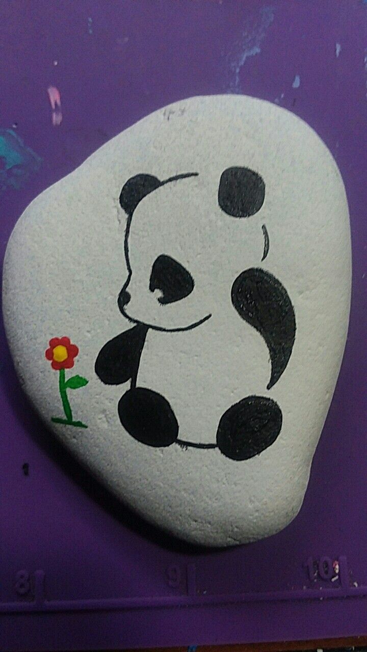 a panda bear painted on the side of a rock with a flower in its mouth
