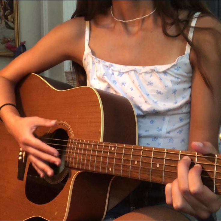 a woman sitting down playing an acoustic guitar