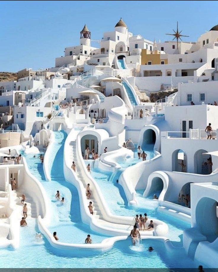 many people are swimming in the water near white buildings and slides that look like they have been built into the hillside