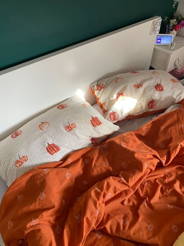 an unmade bed with orange sheets and pumpkins on the pillowcase, next to a night stand