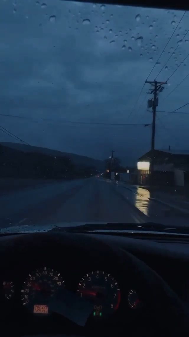 rain is falling on the windshield of a car as it drives down a road at night