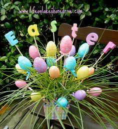 a vase filled with lots of colorful candies on top of a wooden table next to bushes