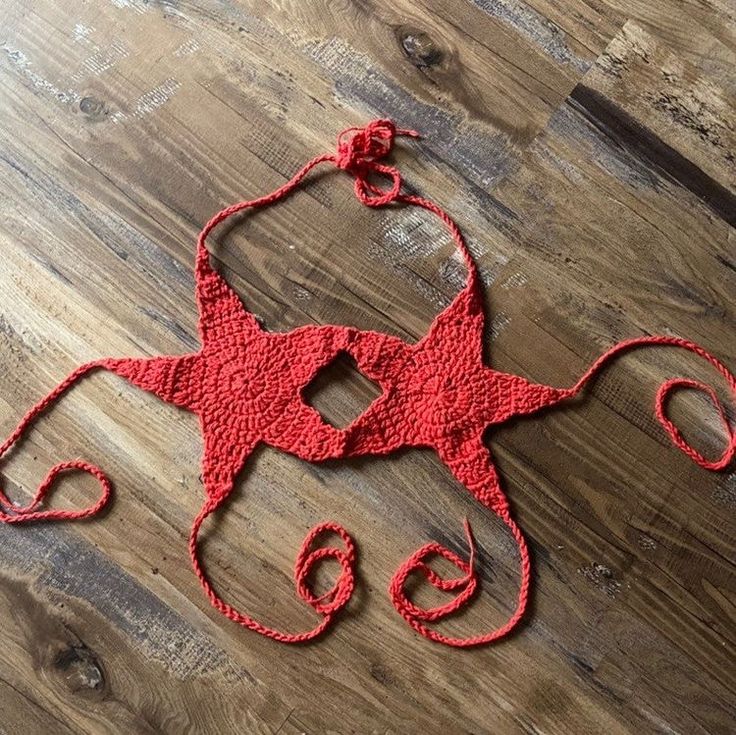 an octopus made out of red yarn sitting on top of a wooden floor next to a pair of scissors