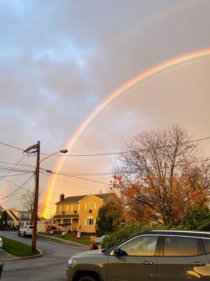 a double rainbow in the sky over a residential area with cars parked on the street