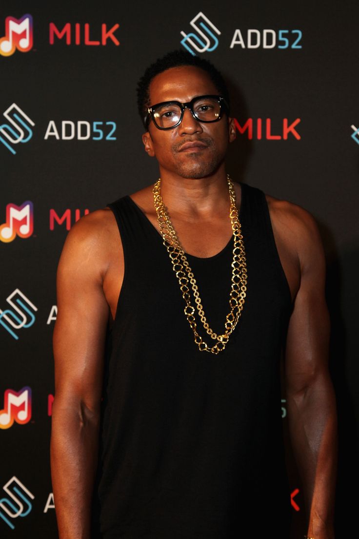 a man wearing glasses standing in front of a wall with the words milk on it