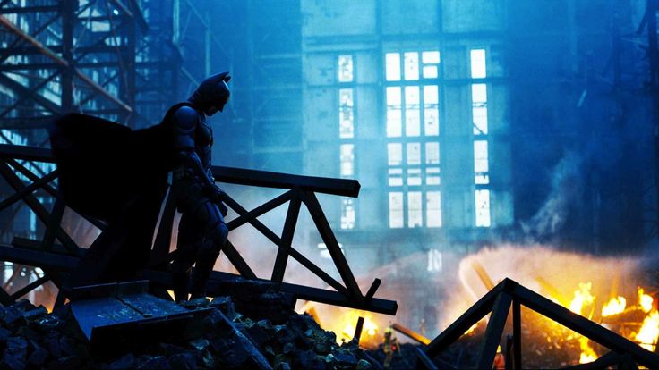 the dark knight stands in front of a pile of rubble and fire with his arm outstretched