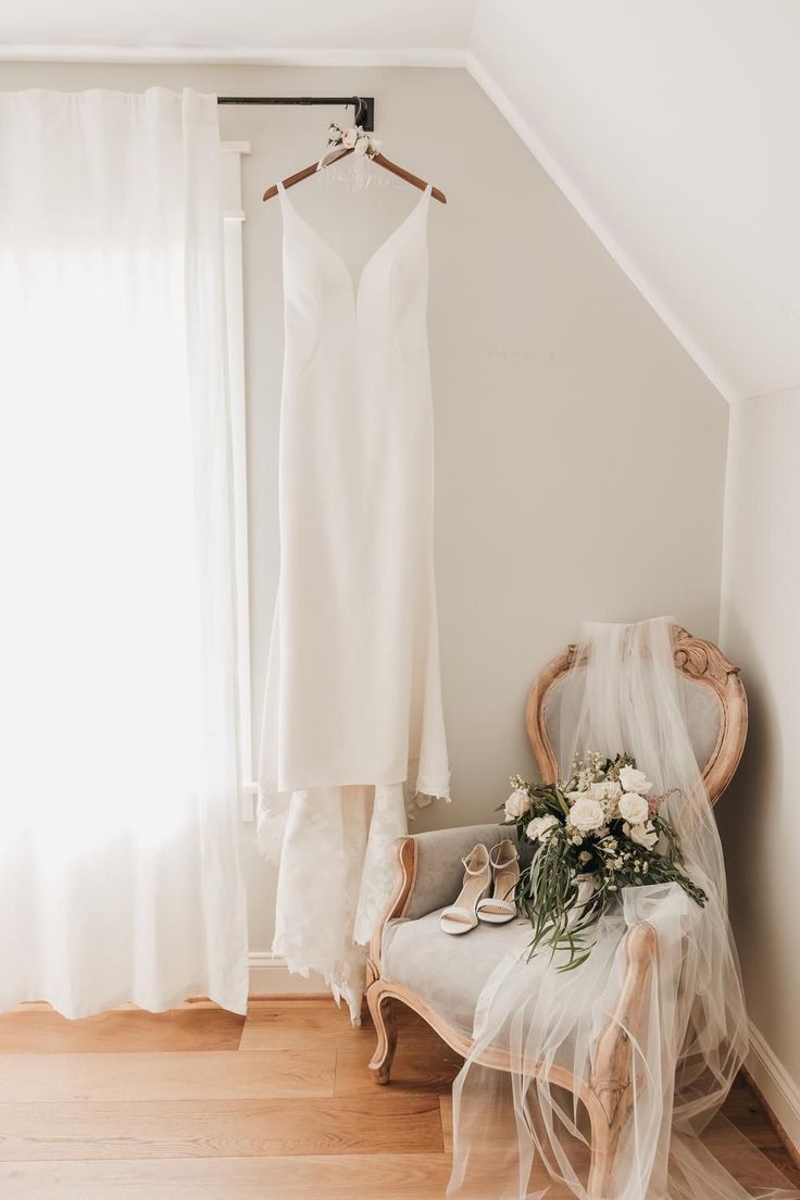 a wedding dress hanging on a hanger next to a brides shoes and bouquet