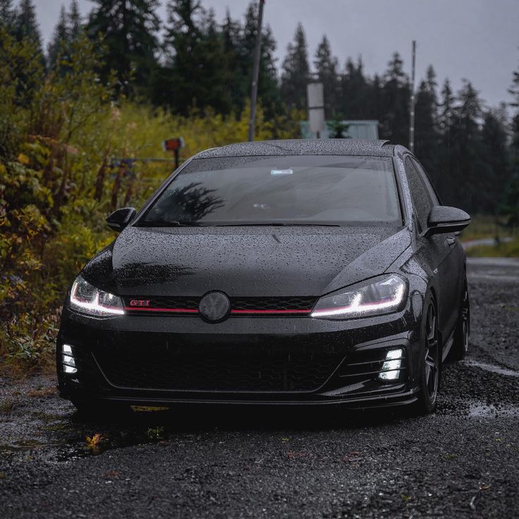 a black car is parked on the side of the road in front of some trees