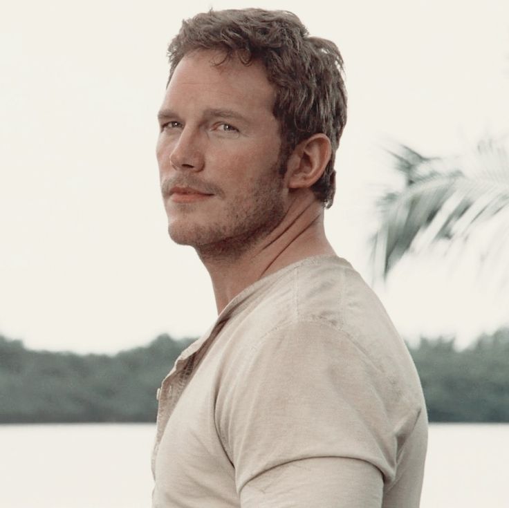 a man standing in front of a body of water wearing a tan shirt and looking off into the distance