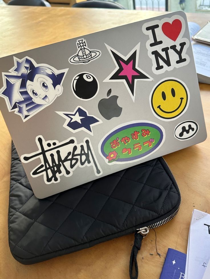 an open laptop computer sitting on top of a wooden table with stickers all over it